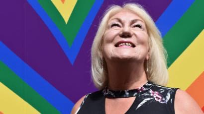 A picture of Carolyn Mercer smiling in front of a pride painted wall