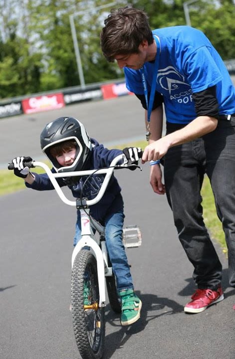 A volunteer helps a young child wearing a helmet to start riding a bike.