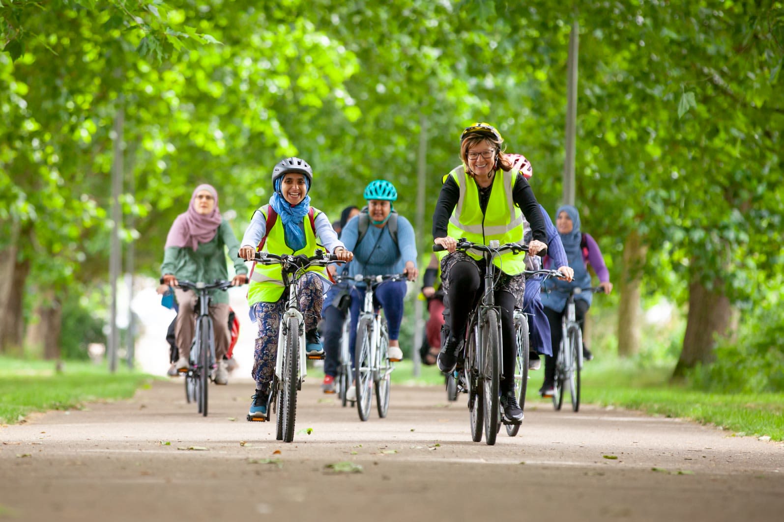 A group of smiling cyclists going uphill in a park lane.