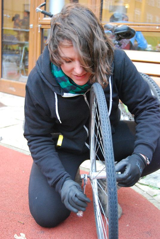 A squatting woman holds a bicyle wheel, tightening a screw