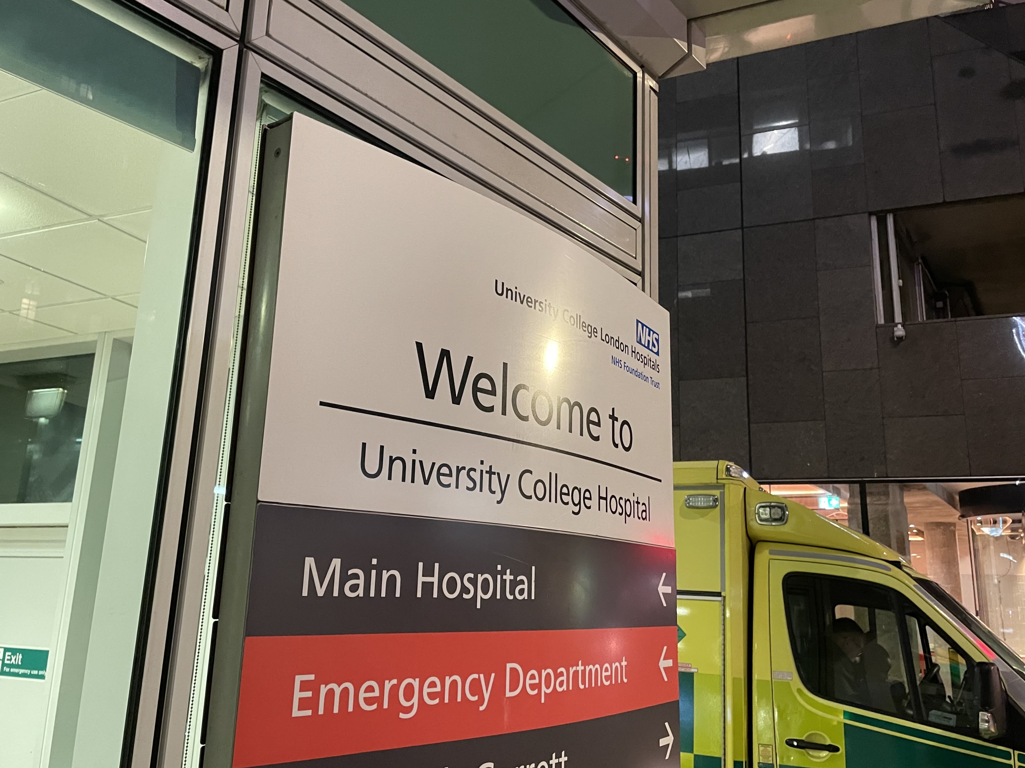 Sign outside a hospital with ambulance in background