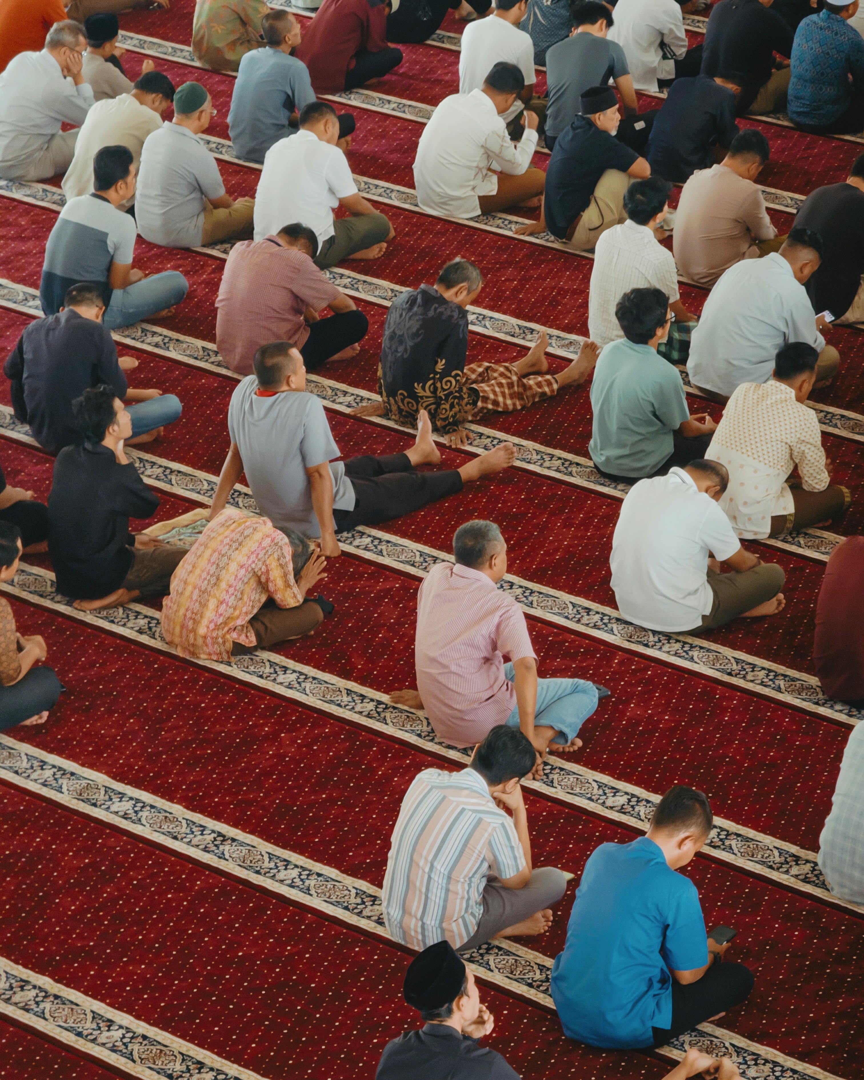 Men praying together on a red carpeted floor.
