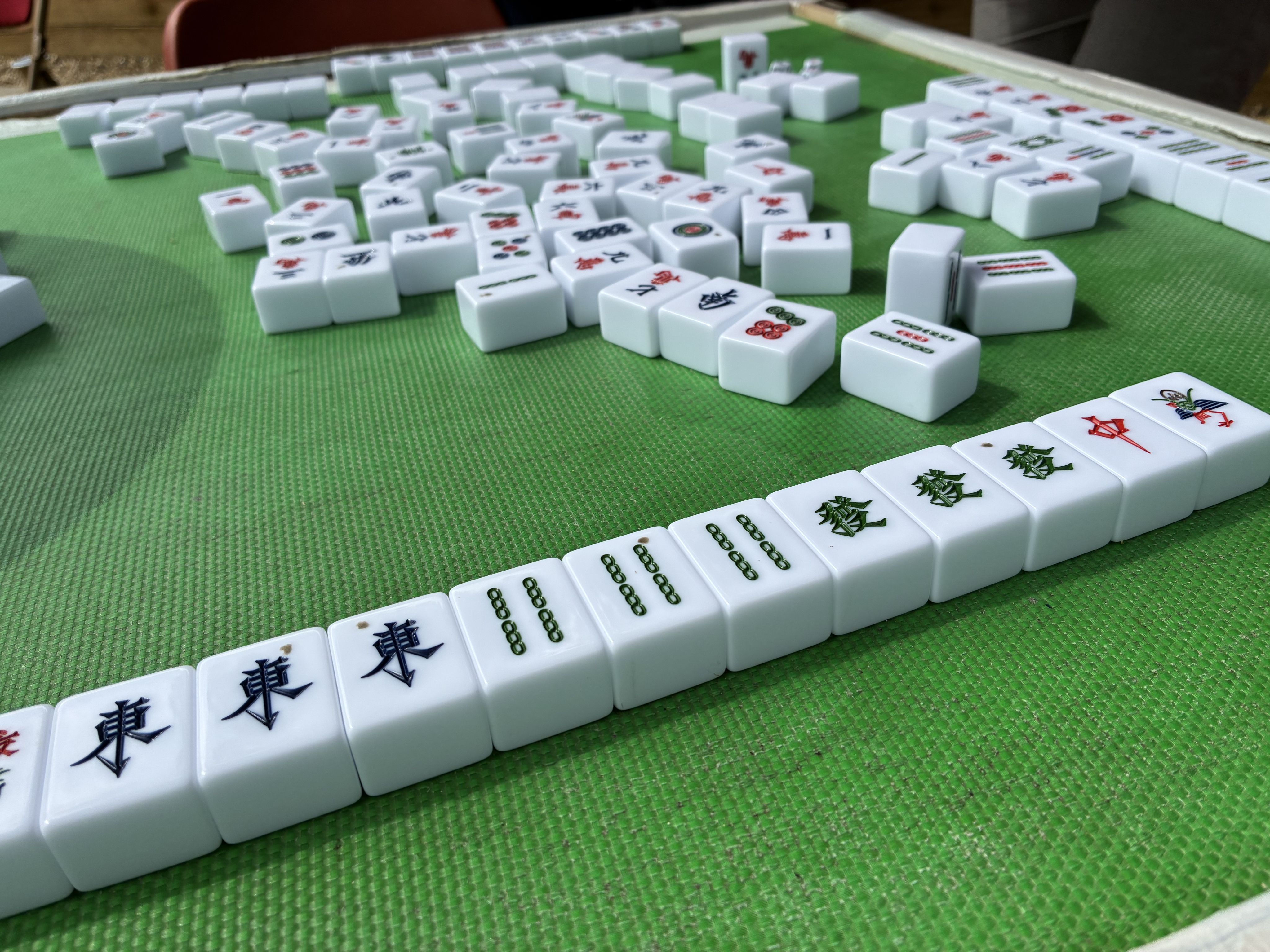 A hand of mahjong tiles laid out next to discarded face-up tiles