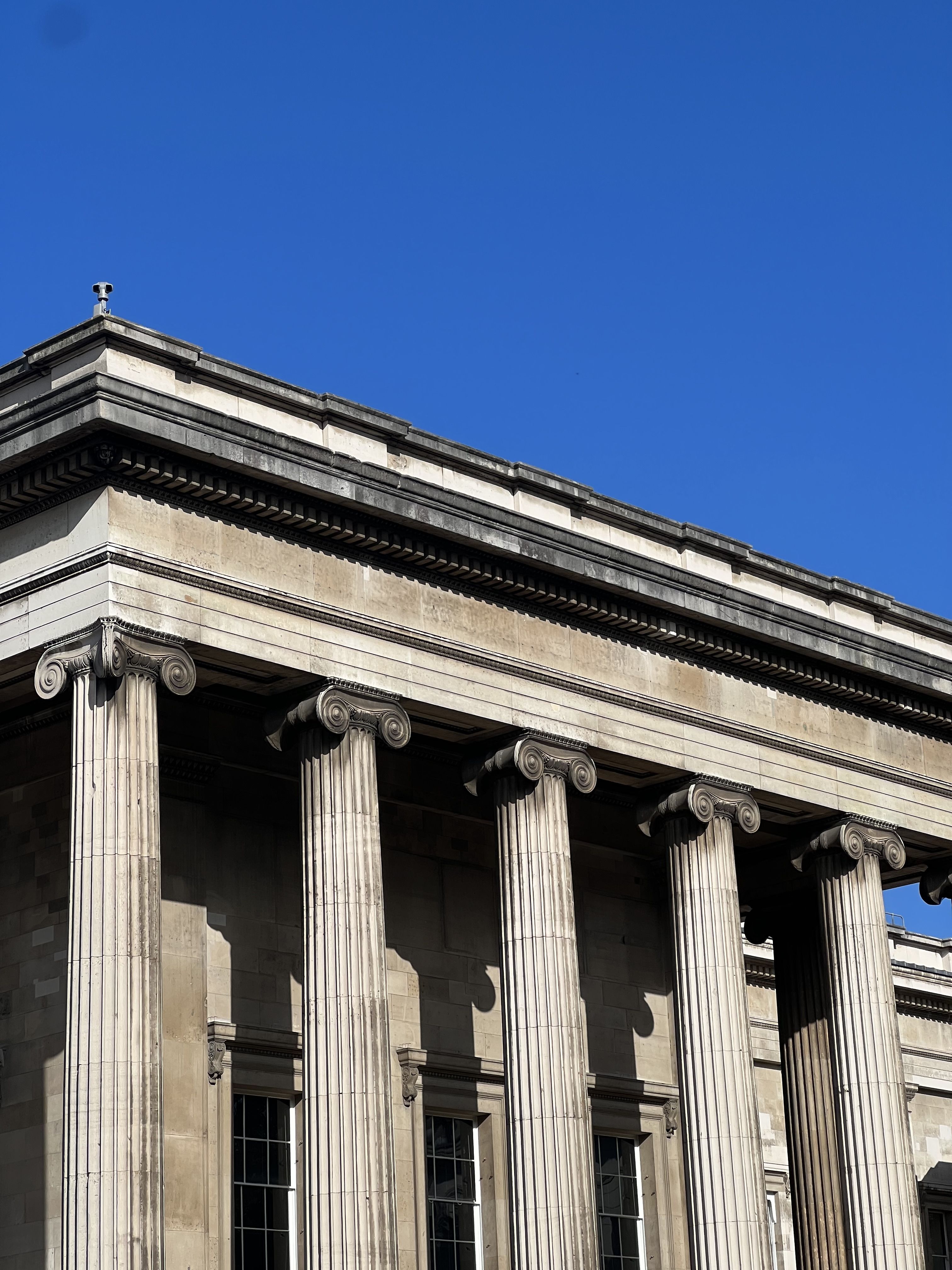 A photo of the pillars of the British museum against a blue sky