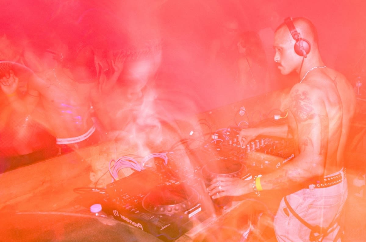 Black and white image of man with his arm raised in the air whilst playing a DJ set