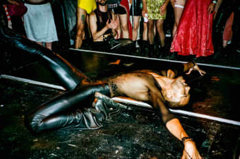 A man in leather trousers and a fishnet top "death dropping" on the floor in front of a crowd