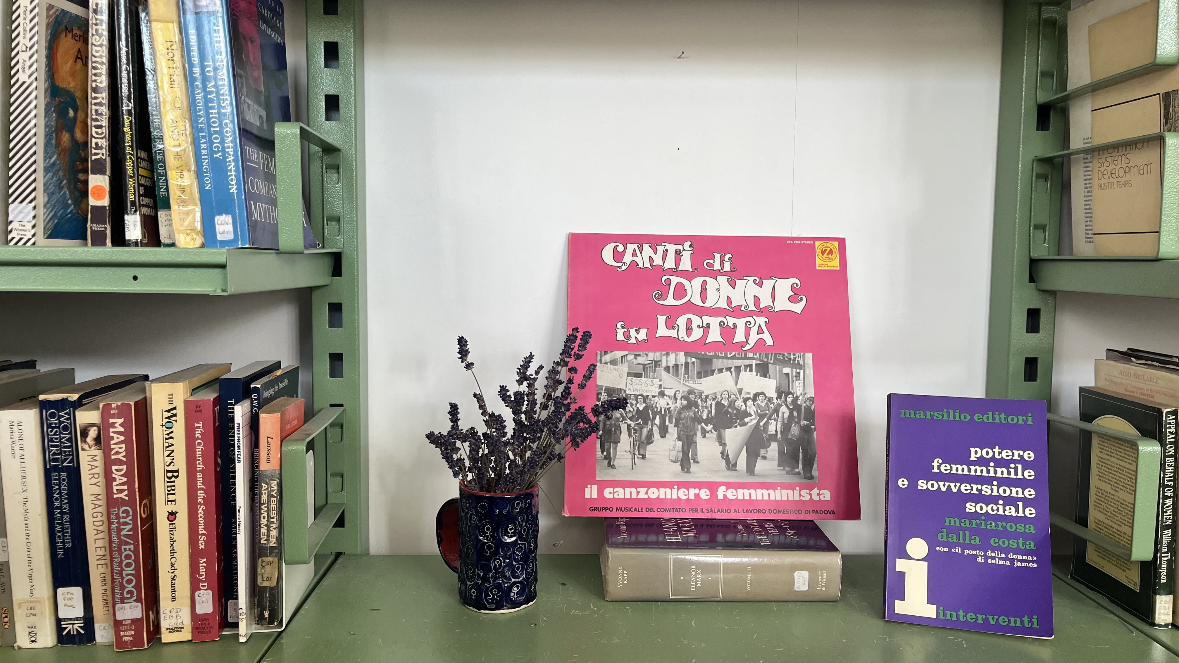A bookshelf display with a pink and purple paperback sat next to a cup of lavendar.