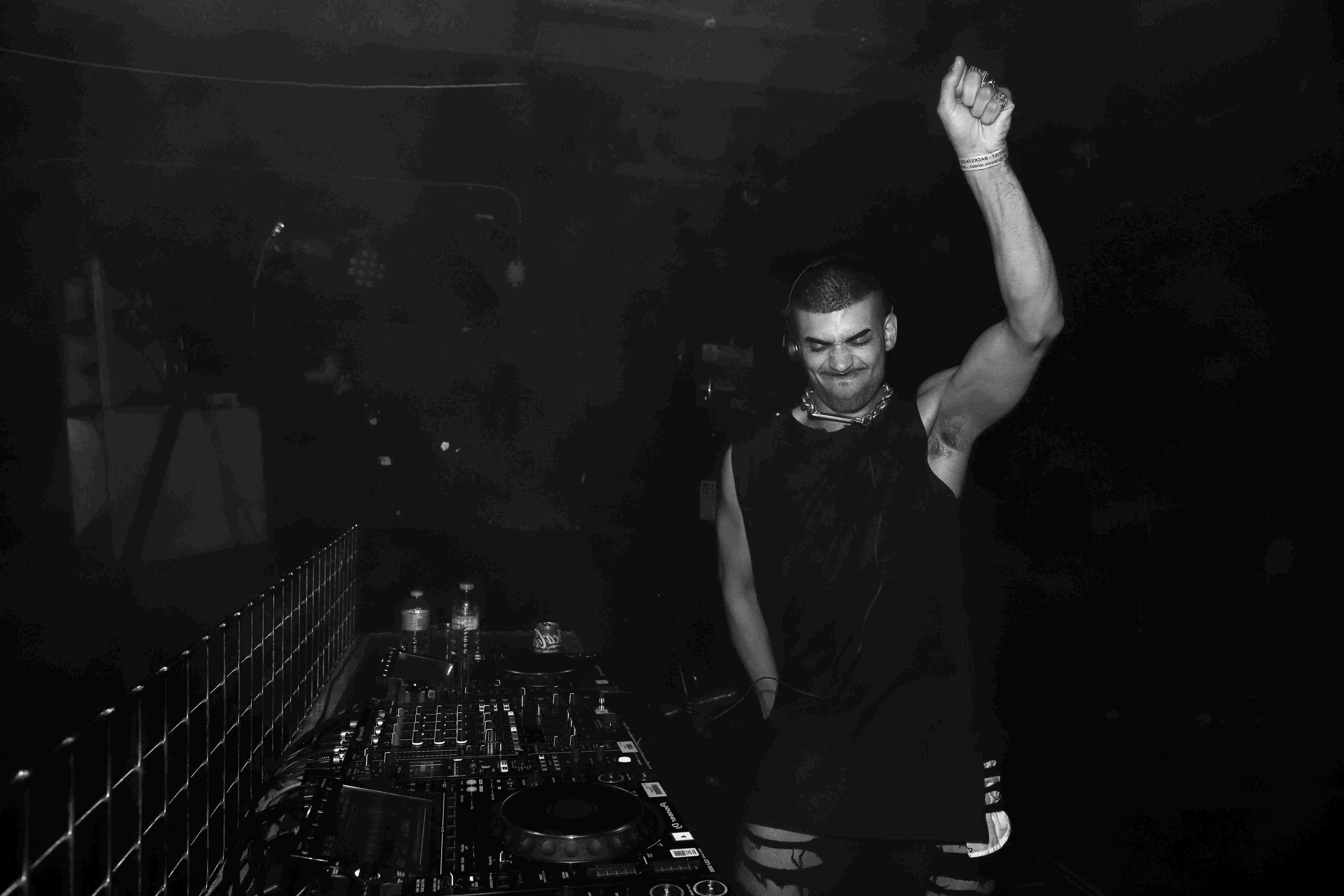 Black and white image of man with his arm raised in the air whilst playing a DJ set