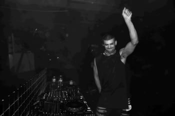 Black and white image of man with his arm raised in the air whilst playing a DJ set