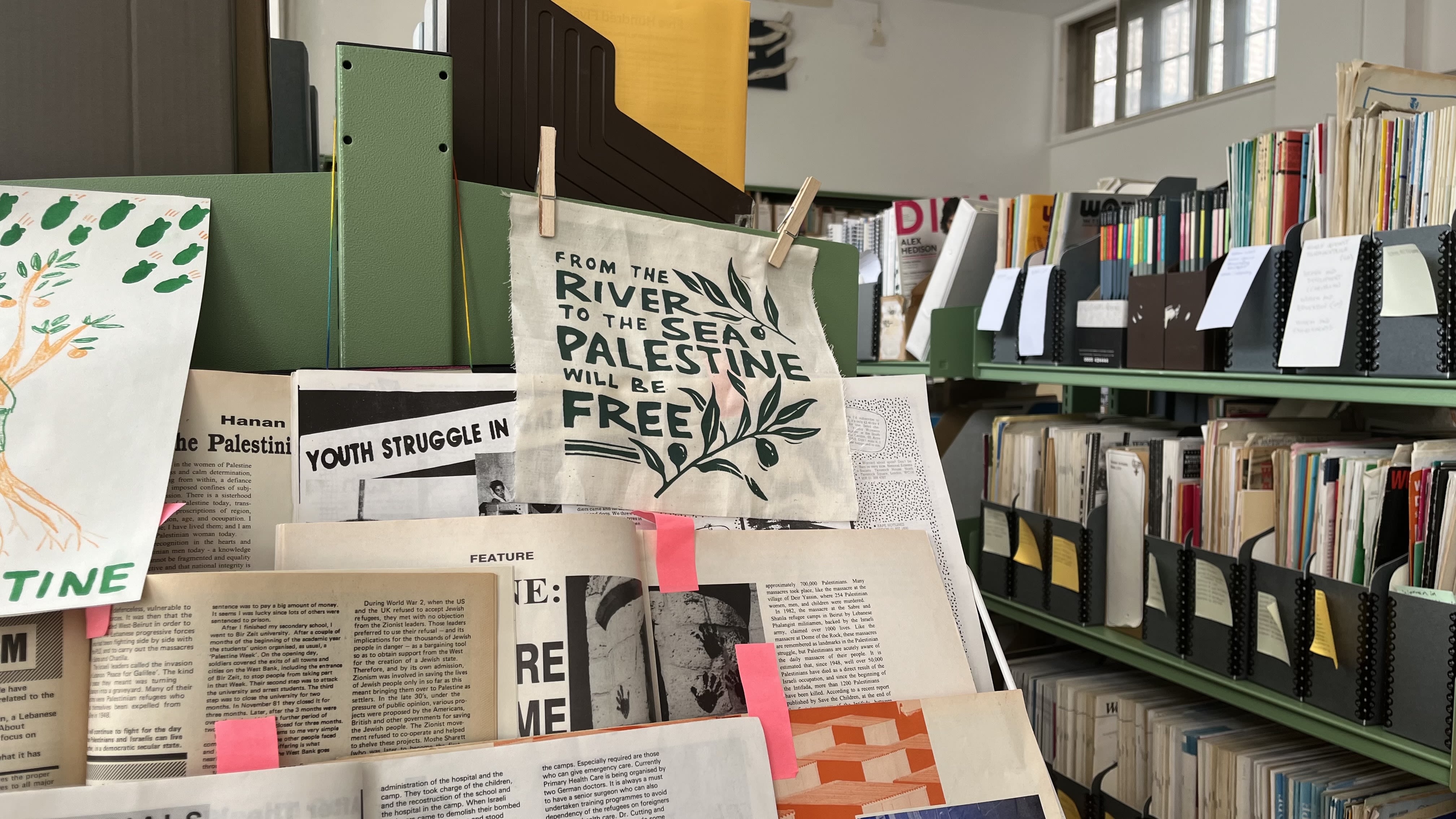 A collection of academic articles and posters about the Palestine-Israel conflict are propped up against the backdrop of a library archive