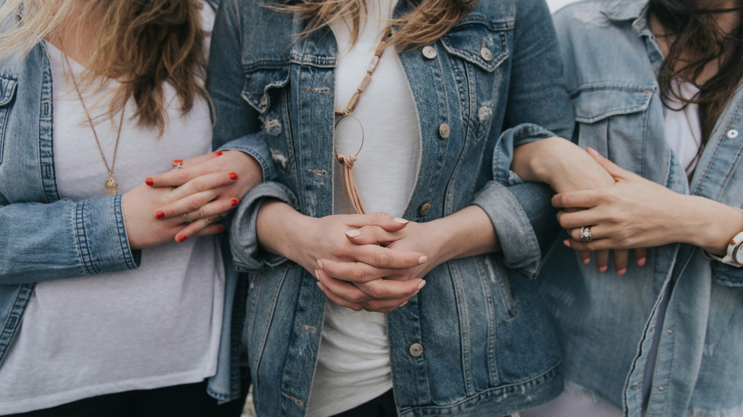women wearing blue denim jackets and white tops linking arms