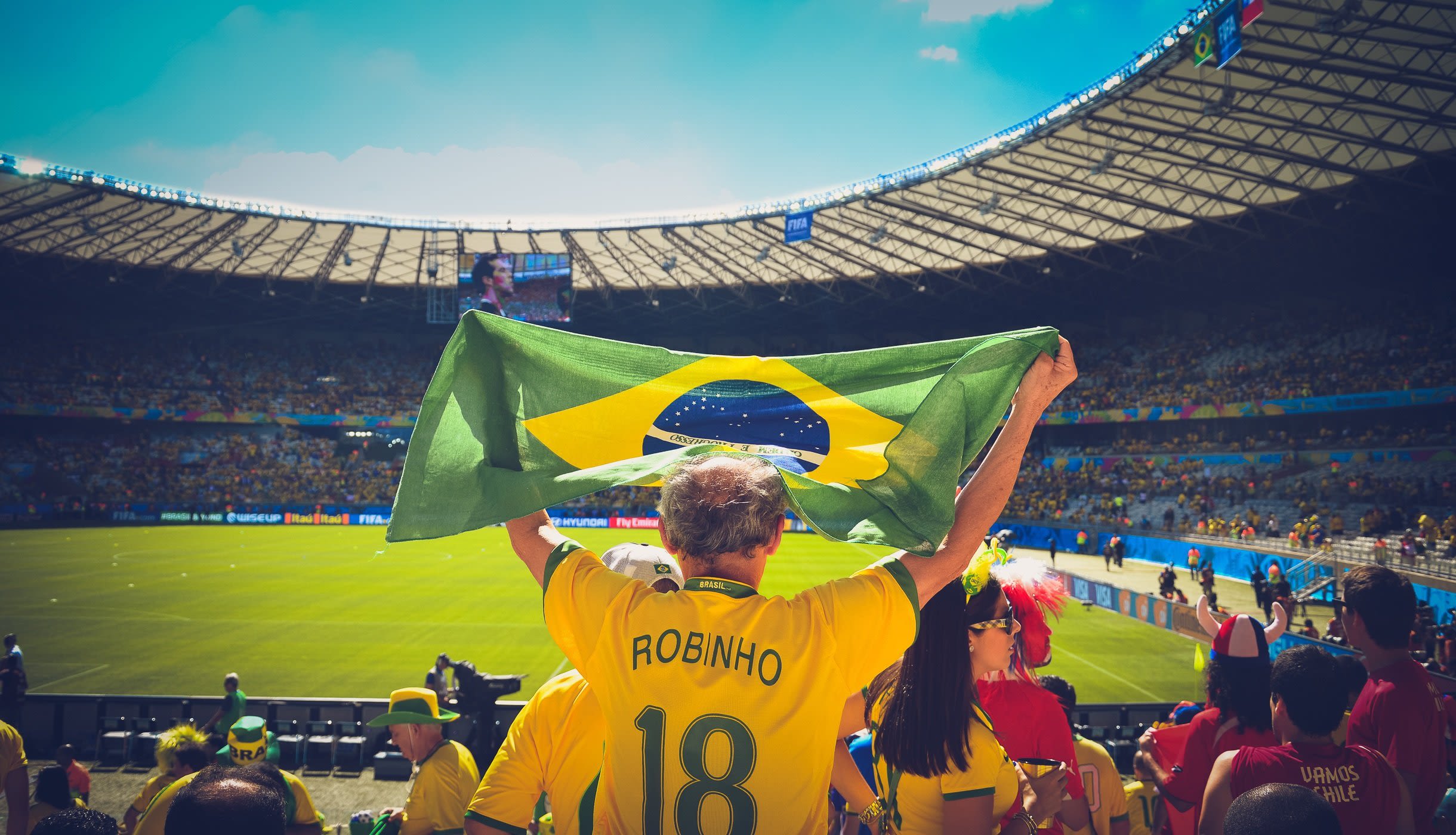 Brazilian fan holding Brazil flag wearing Robinho 18 yellow shirt in football stadium