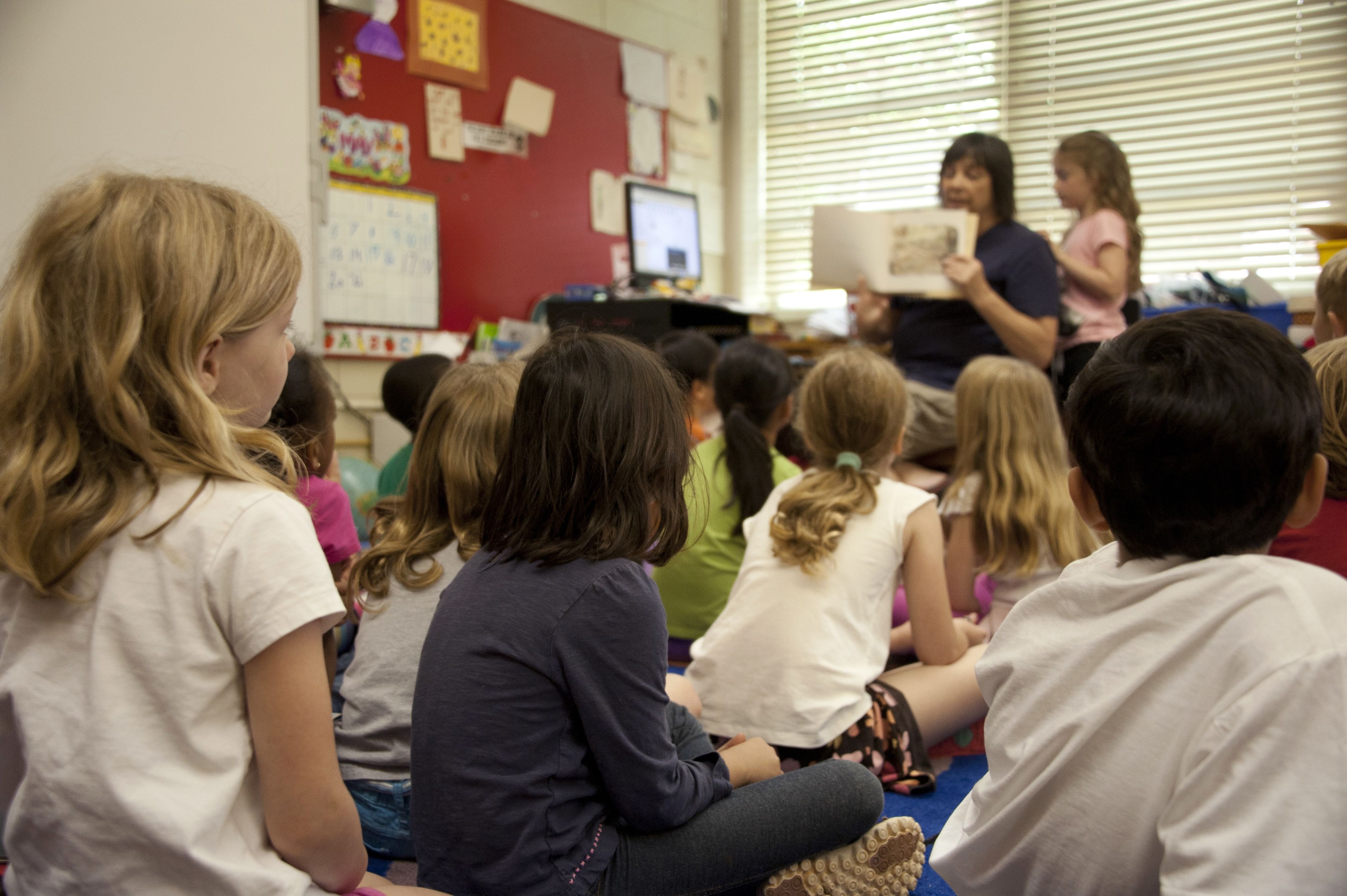 Female teacher reads a library book to a young students