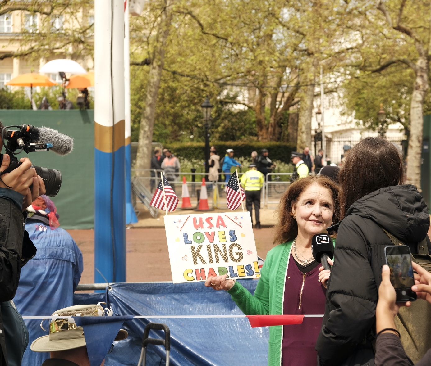 A women with a sign reading "USA loves King Charles" is interviewed by a TV reporter