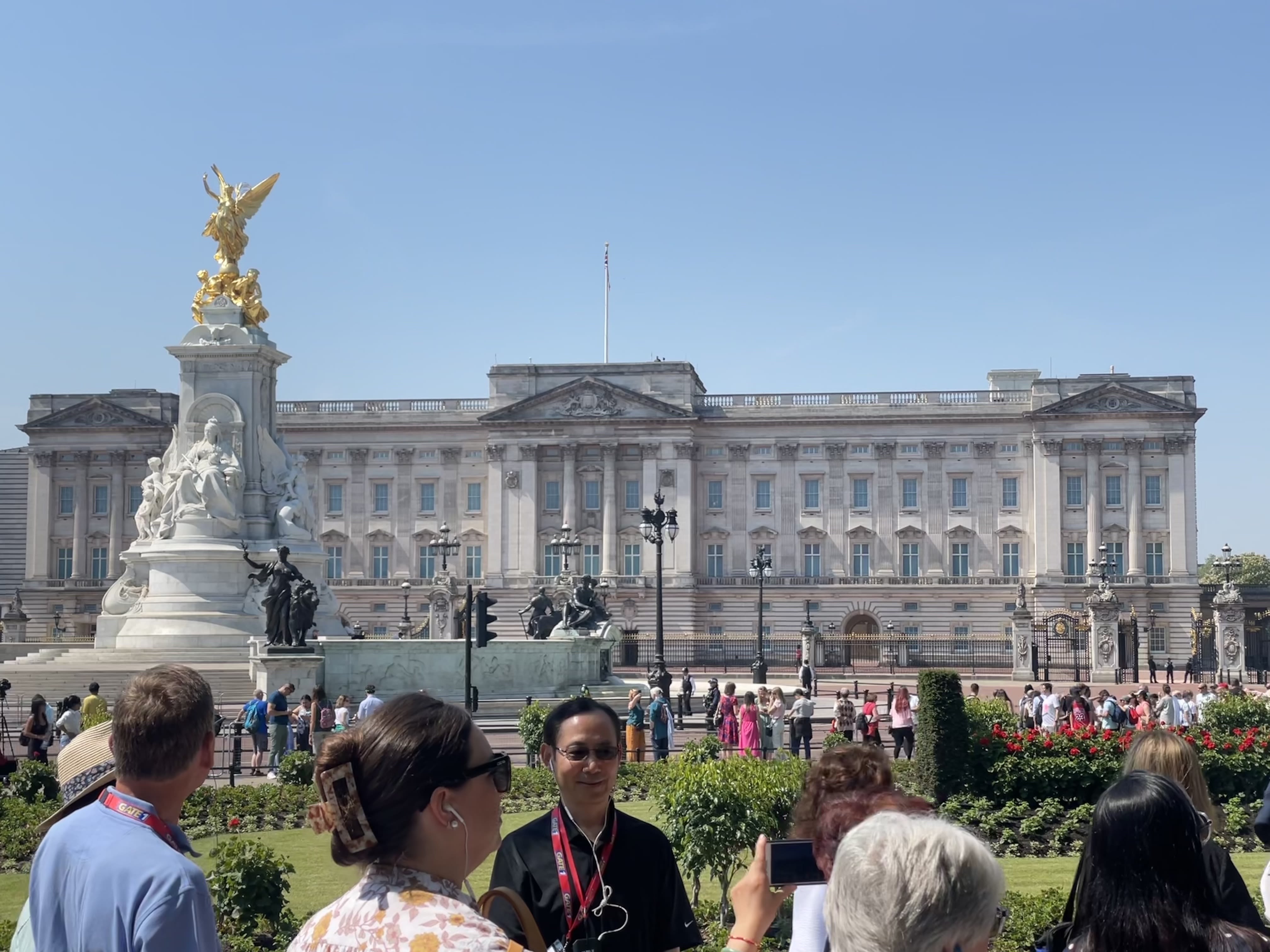 A tourist poses outside Buckingham Palace on a sunny day