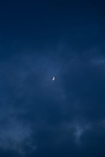 A serene view of a crescent moon amidst dark clouds over Denmark's night sky.
