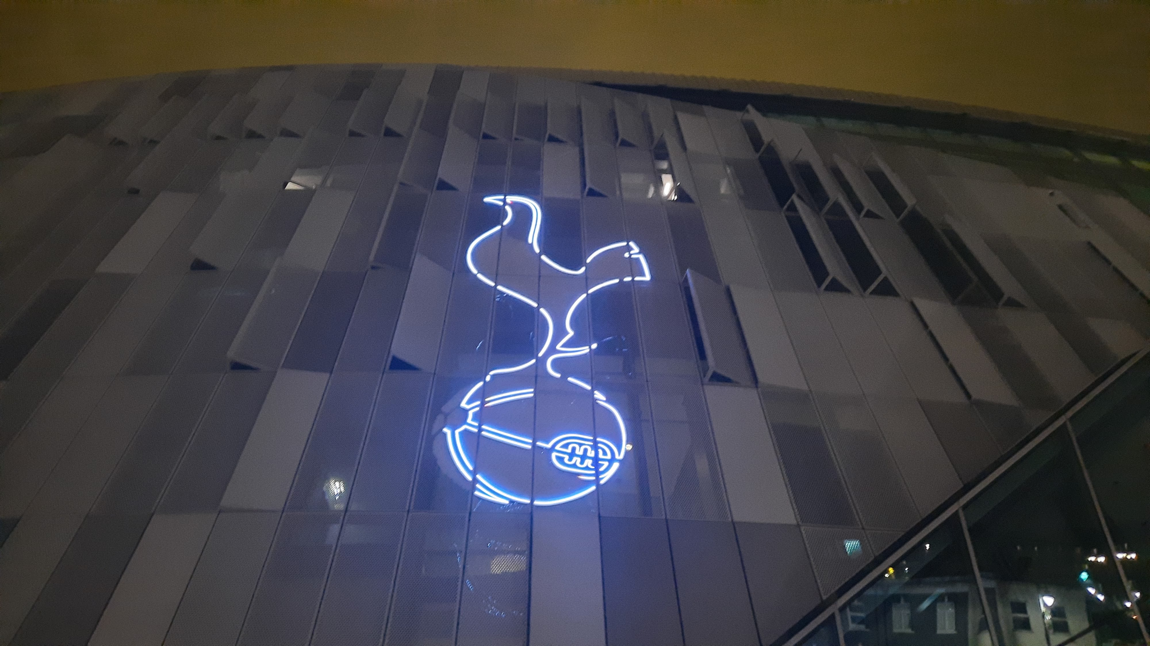 A picture of the Tottenham Hotspur badge lit up in blue on the front of their stadium